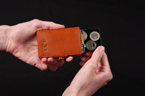 Tony Perotti black aluminium tray for Furbo, pulled from a Cognac Furbo card holder held in two hands, holding coins and a key